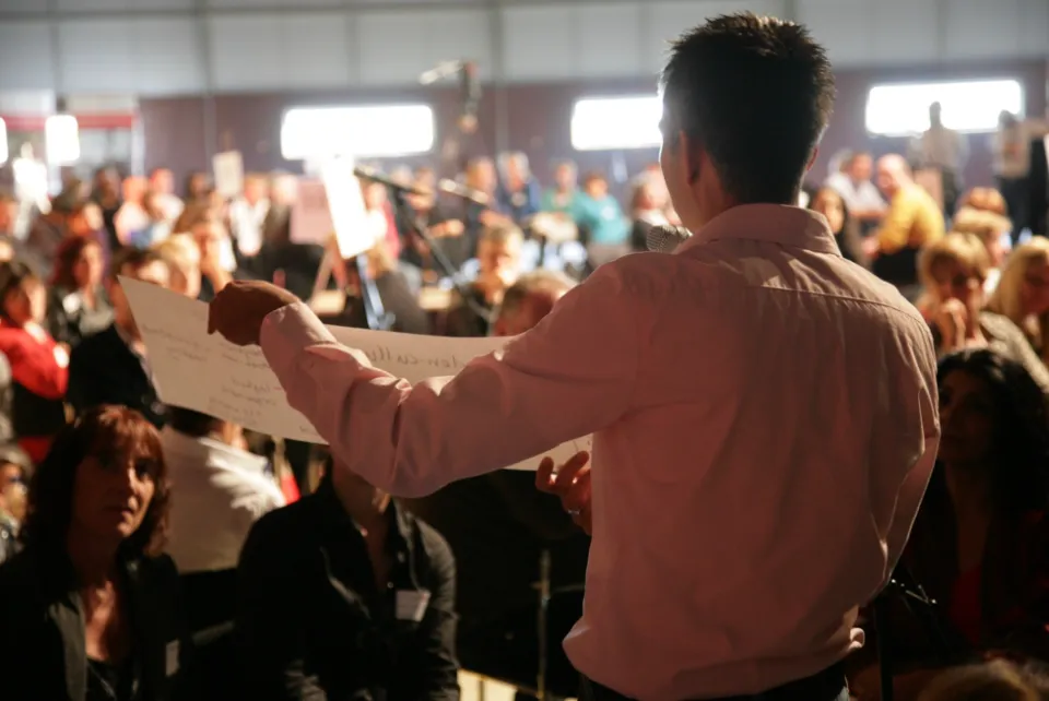 Facilitator holding up a sheet of paper in front of a seated audience